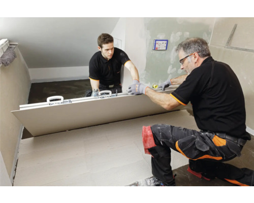 Zwei Handwerker verlegen eine große Fliese im Innenraum.