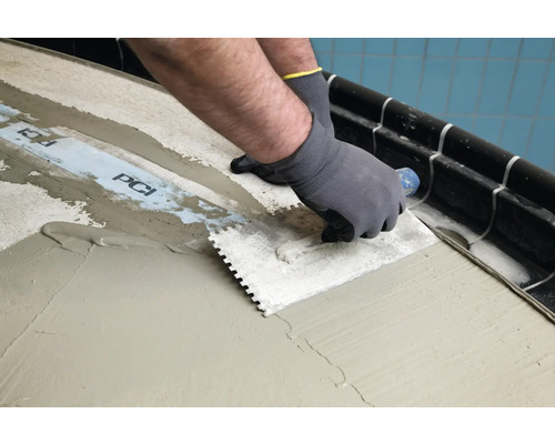 Fliesenleger trägt mit einer Zahnspachtel Kleber auf einen Untergrund auf