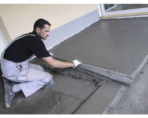 Ein Mann glättet Estrich mit einer Richtlatte auf einer Terrasse.