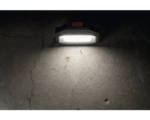 Metabo Logo. Auf dem Bild ist eine Arbeitsleuchte zu sehen, die einen Betonboden beleuchtet.