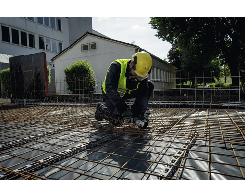 Ein Bauarbeiter kniet auf einem Gitterrost und arbeitet mit einem Winkelschleifer.