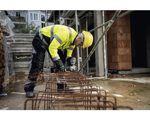 Bauarbeiter mit Schutzhelm und Schutzweste bei der Arbeit mit einem Winkelschleifer zum Schneiden von Metall auf einer Baustelle