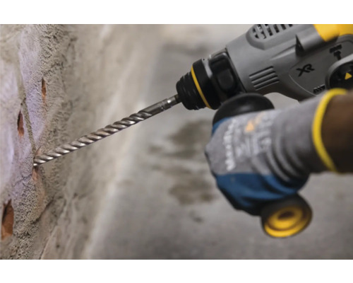 Eine Person bohrt mit einer Bohrmaschine Löcher in eine Ziegelwand.