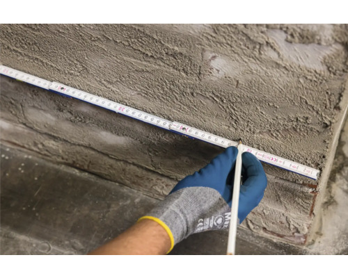 Hand mit Bleistift markiert eine Messung auf einem Gliedermaßstab an einer Wand