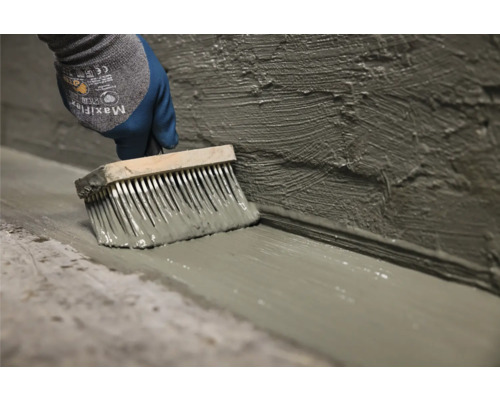 Eine Person trägt mit einem Pinsel eine Abdichtung auf Wand und Boden auf.