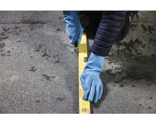 Eine Person mit Schutzhandschuhen schneidet mit einem Cuttermesser entlang einer Wasserwaage.