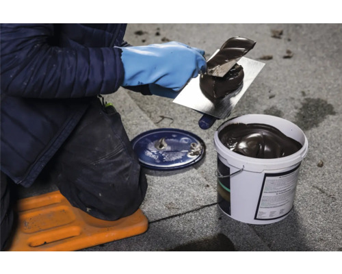 Dachdecker trägt mit einer Spachtelmasse Dachabdichtung auf ein Dach auf.