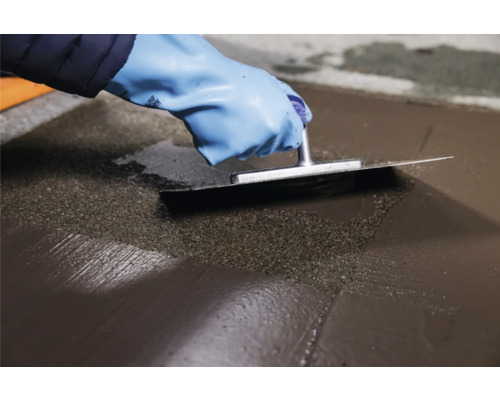 Eine Person glättet eine Bodenspachtelmasse mit einer Glättkelle.