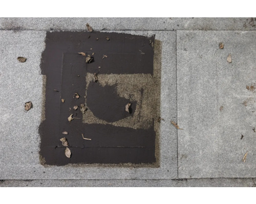 Detailansicht einer reparierten Pflasterfläche mit Bitumenflicken auf Pflastersteinen.