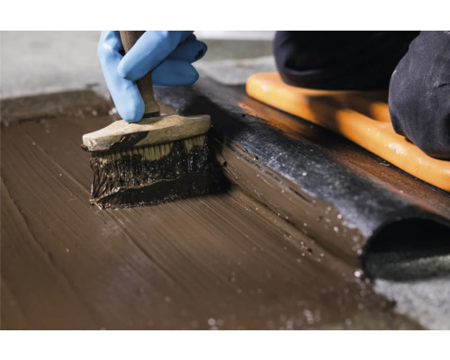 Auftragen von Dichtmasse mit einem Pinsel auf eine Dachbahn.