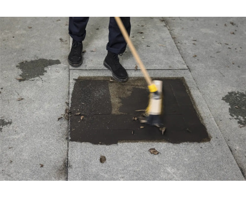 Eine Person reinigt eine Dachrinne mit einer Bürste auf einem Dach.