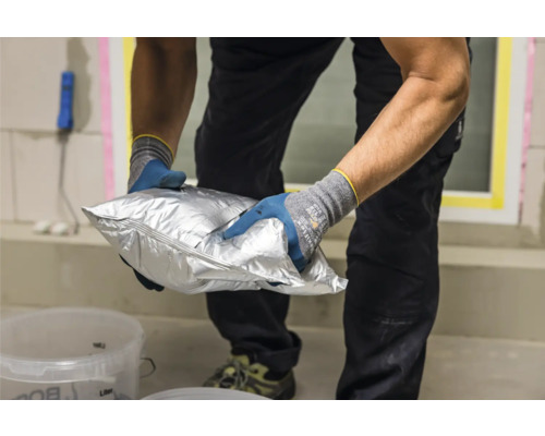 Eine Person hält eine silberne Tüte mit Material für Bauarbeiten.