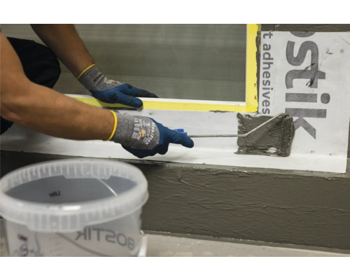 Person trägt Dichtstoff mit einer Rolle auf, mit Bostik Logo im Hintergrund