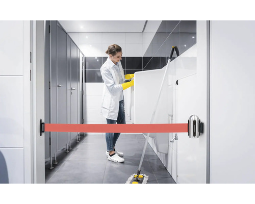 Szene einer Reinigungskraft, die eine Herrentoilette mit einem Absperrband versehen hat, während sie die Urinale reinigt.