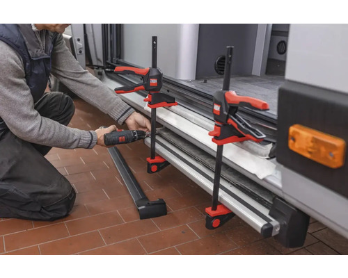 Handwerker befestigt eine Leiste mit einer Schraube und Schraubzwingen an einem Fahrzeug.