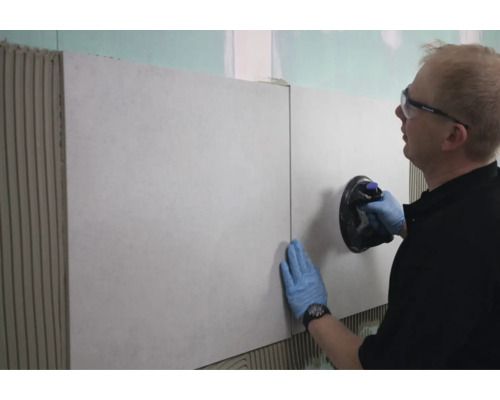 Fliesenleger verlegt Fliesen an der Wand mit Saugheber