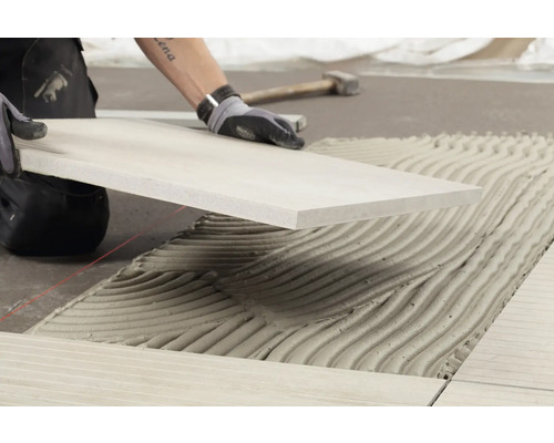 Fliesenleger bei der Arbeit: Verlegen einer Fliese auf Klebemörtel