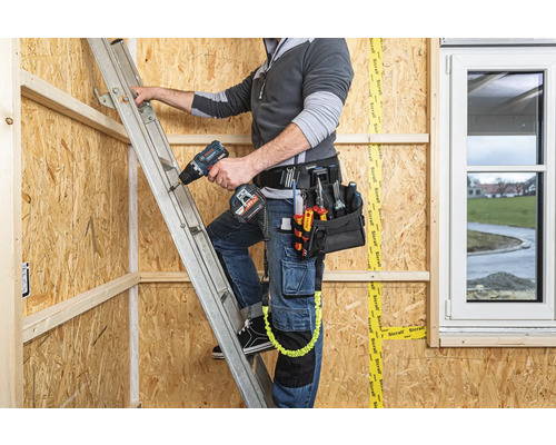 Handwerker auf einer Leiter mit Werkzeug und Bohrmaschine in einem Rohbau