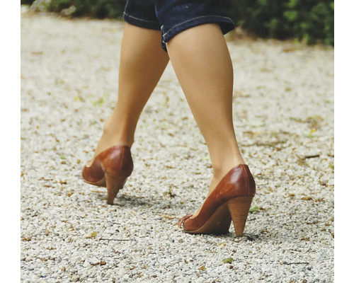 Frau geht in Lederschuhen mit Absatz auf Kies