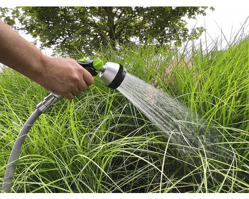 Eine Hand hält einen Gartenschlauch, mit dem die Gartenpflanzen bewässert werden.