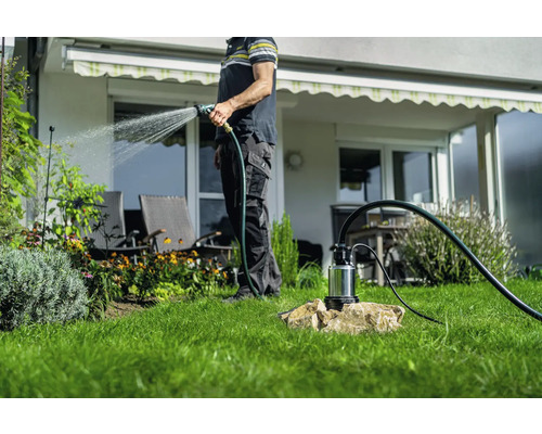 Person bewässert Garten mit Gartenpumpe und Gartenschlauch