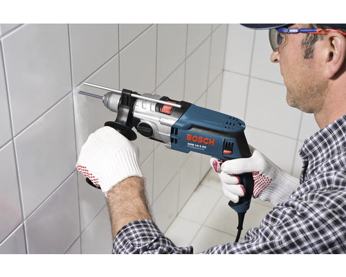 Ein Mann bohrt mit einer Bosch Schlagbohrmaschine ein Loch in eine geflieste Wand.