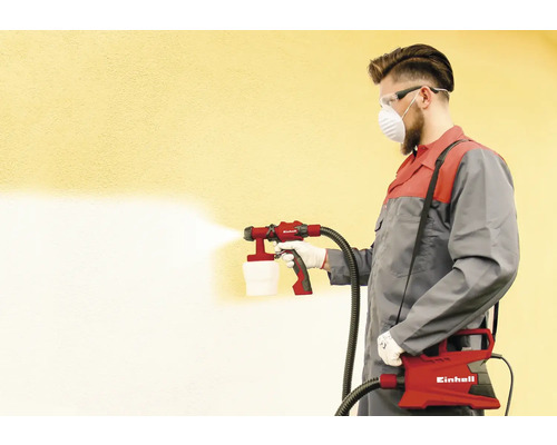Mann mit Farbsprühsystem beim Sprühen einer Wand