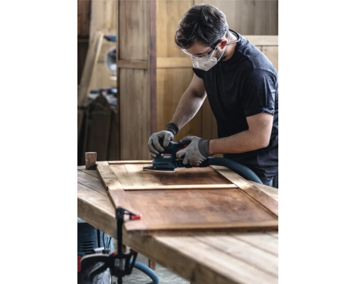 Mann schleift Holztür mit Schwingschleifer in Werkstatt