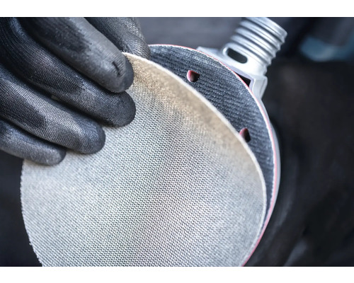 Person mit Schutzhandschuhen hält Schleifscheibe