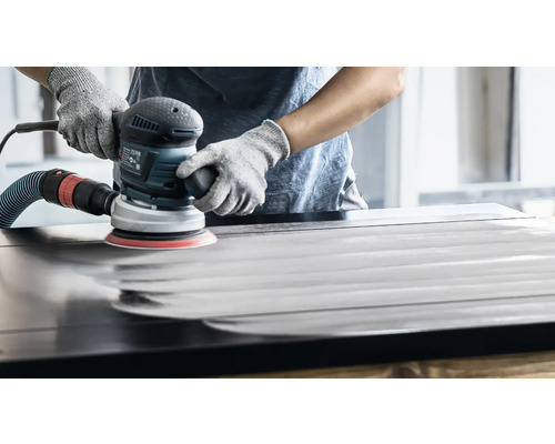 Eine Person schleift eine Holzoberfläche mit einem Exzenterschleifer.