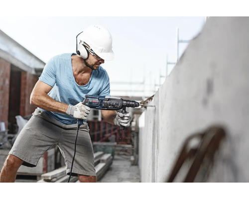 Handwerker bohrt mit einem Bohrhammer in eine Betonwand. Er trägt Schutzkleidung.