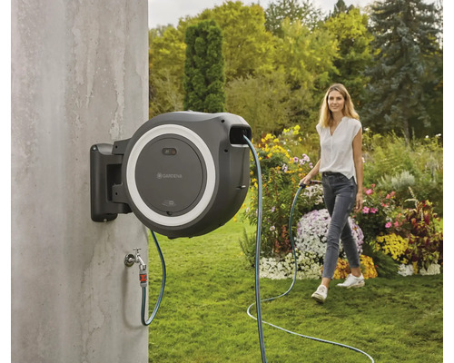 Garten Szene mit einer Frau, die einen Garten mit einem Gartenschlauch bewässert, der an einer Schlauchbox befestigt ist.