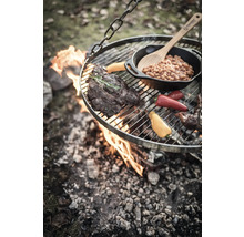 Hängender Grill über offenem Feuer mit Steak, Gemüse und Bohnen in einer Pfanne.