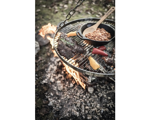 Hängender Grill über offenem Feuer mit Steak, Gemüse und Bohnen in einer Pfanne.