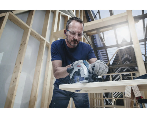 Ein Mann sägt mit einer Handkreissäge ein Holzbrett in einer Baustelle