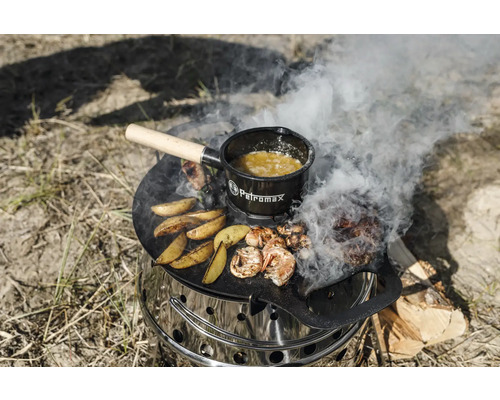 Ein Petromax Atago Grill mit Grillplatte, darauf Speisen und ein Petromax Topf