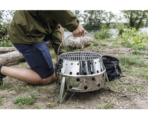 Person trägt einen tragbaren Edelstahlgrill im Freien.