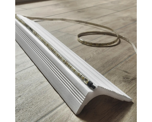 Weiße Zierleiste mit LED-Streifen auf einem Holzboden.