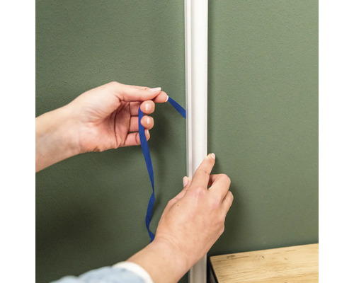 Hände messen mit einem Band den Abstand zur Zierleiste