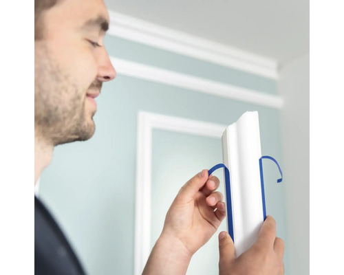 Mann entfernt blaues Klebeband von einer weißen Zierleiste.