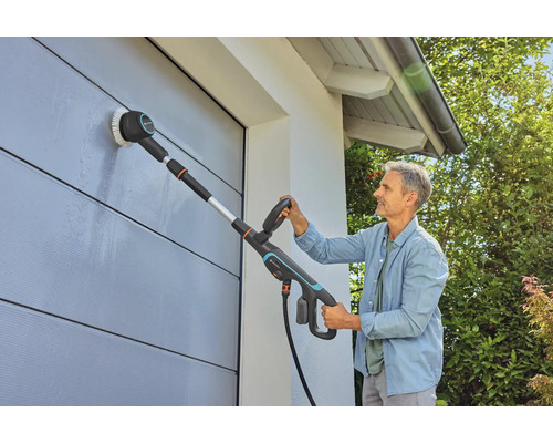 Mann reinigt Hauswand mit einer Bürste und Teleskopstiel