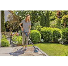 Frau reinigt Terrasse mit elektrischer Bürste im Garten.