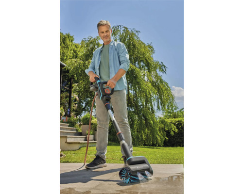 Ein Mann benutzt eine Gardena Bürste zum Reinigen einer Steinoberfläche im Freien.