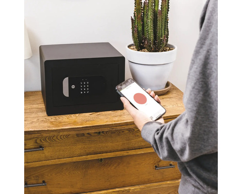 Schwarzer Tresor mit digitalem Display und Smartphone-Steuerung auf Holzkommode.