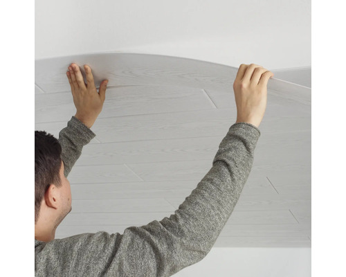 Person montiert eine Deckenpaneele mit Holzoptik an einer Zimmerdecke.