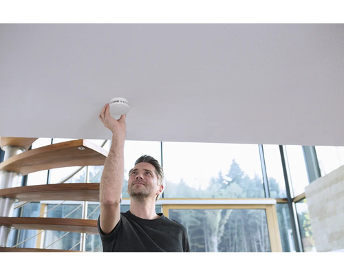 Mann montiert Rauchmelder an der Decke