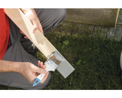 Mann streicht Holzbrett mit Pinsel und Farbe