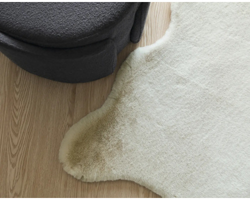 Dekorative Tierfellimitation neben einem grauen Sitzhocker auf einem Holzboden.