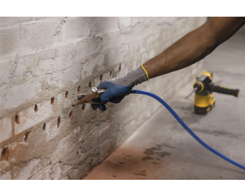 Mann injiziert Flüssigkeit in eine Ziegelwand mit Injektionslanze