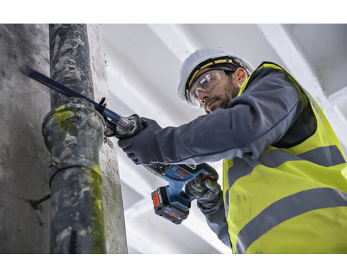 Ein Mann schneidet mit einer Akku-Säbelsäge ein Rohr.